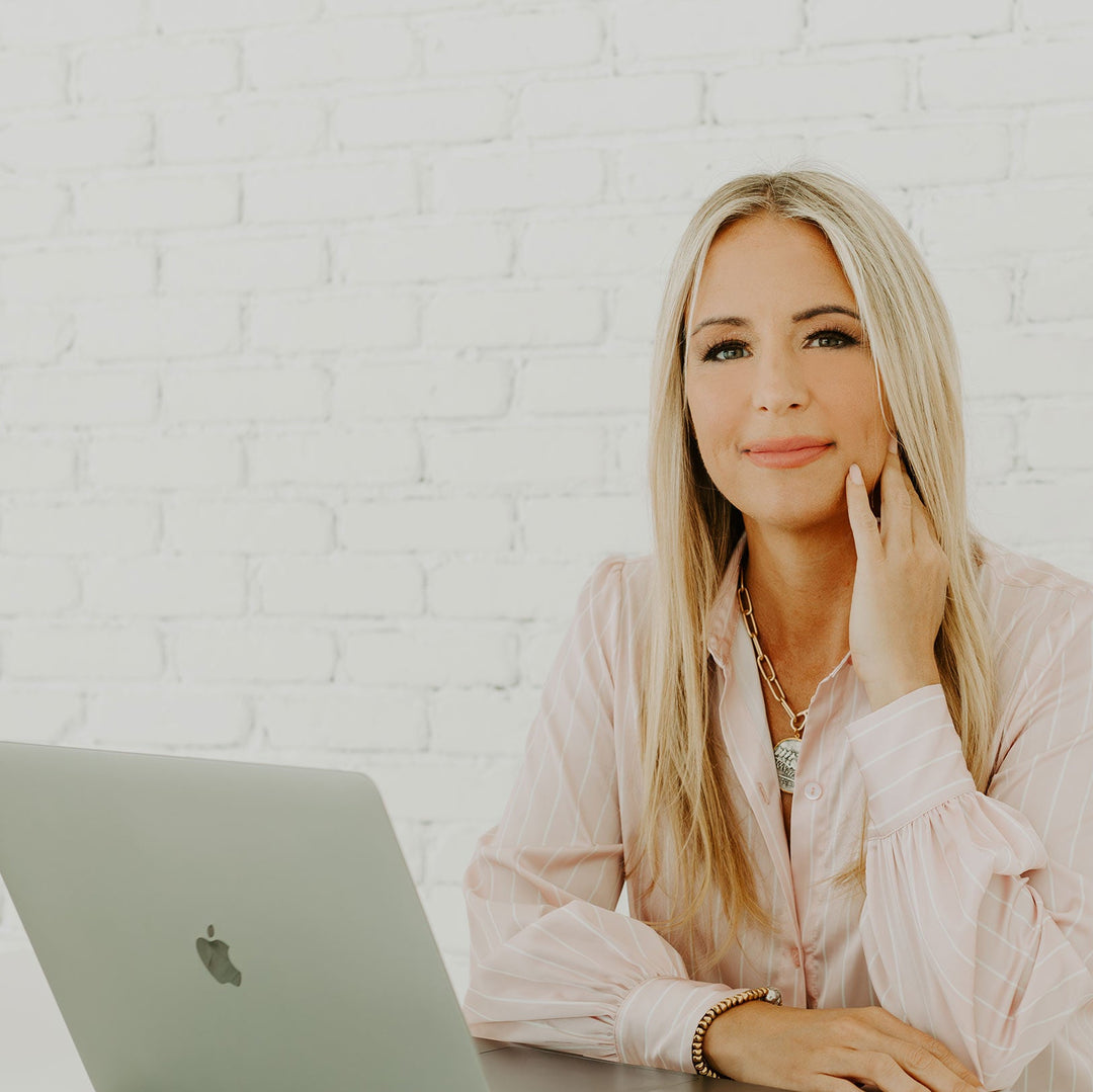 Woman sitting at a desk with a laptop in a bright room.